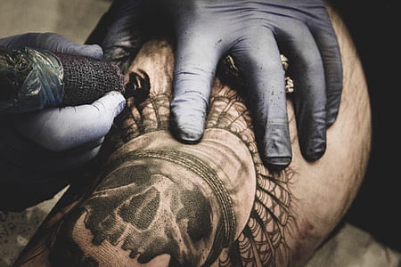 person tattooing person's skin with skull at daytime thumbnail