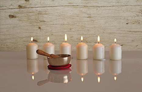 six white pillar candles behind brass-colored bowl reflecting on white surface thumbnail
