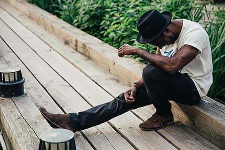 A young African American man wearing black hat laughing while sitting on a sidewalk thumbnail