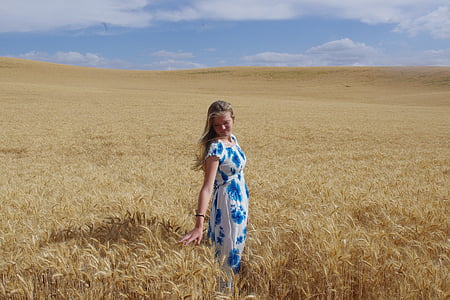 woman wearing white and blue floral cap-sleeved dress standing beside and holding wheat field thumbnail