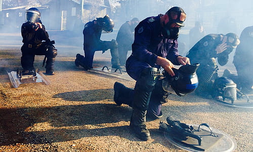 man wearing gas mask kneeling about to wear helmet near men thumbnail