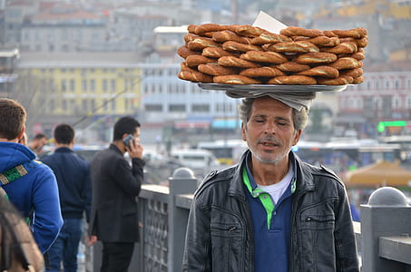 man in black leather zip-up jacket with tray of bread on his head during daytime thumbnail