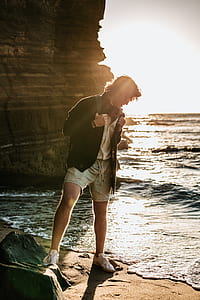 man in black coat near seashore behind brown rock formation thumbnail