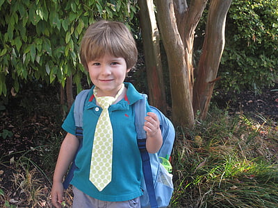 boy in blue polo shirt with backpack near tree thumbnail