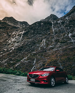 photo of red Mazda sedan near rocky mountain under cloudy blue sky thumbnail