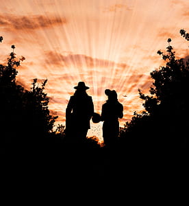 Silhouette Photo of Man and Woman Wearing Hat Standing Between Trees during Golden Hour thumbnail