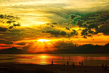 sunset over mountain in sea with people on beach thumbnail