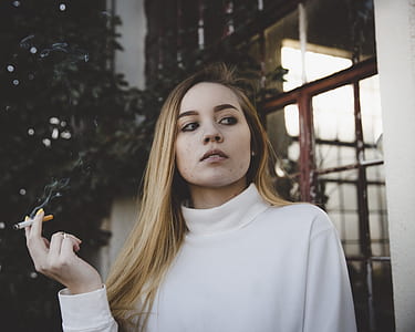 woman smoking outside house near trees thumbnail