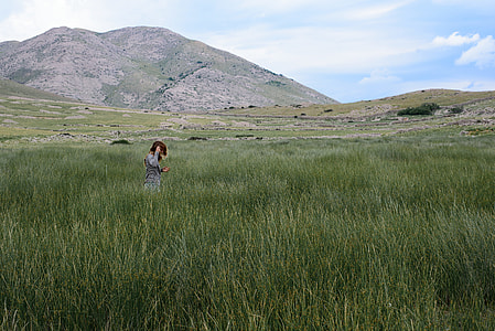 person wearing gray top walking on green grassland near mountain range thumbnail