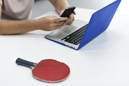 person holding smartphone beside MacBook and table tennis paddle thumbnail