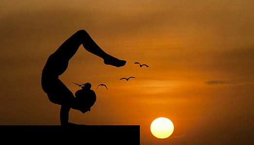 Woman doing an acrobatic yoga pose, silhouetted against sunset. thumbnail