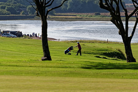 man pushing trolley golf bag in an open field at daytime thumbnail
