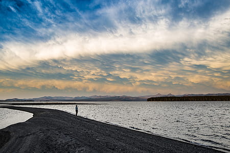 photo of person standing on sandbar while looking on body of water during daytime thumbnail