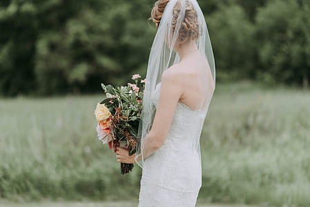 woman in white strapless wedding dress on green grass field holding flower bouquet thumbnail