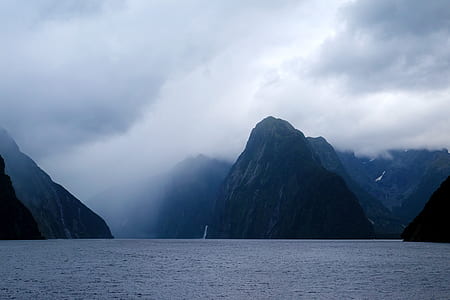 body of water near high mountains under white sky at daytime thumbnail