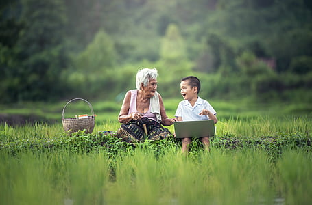 boy with laptop sitting beside white haired woman on green field thumbnail