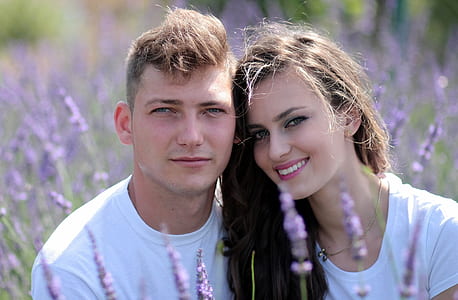 shallow focus photography of man and woman wearing white crew-neck tops surrounded by purple flowers thumbnail