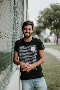 man standing beside gray chain link fence while smiling thumbnail