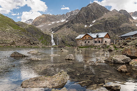 brown concrete house near river and mountains at daytime thumbnail