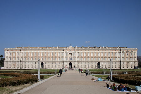 person walking toward white and brown concrete building under blue sky at daytime thumbnail