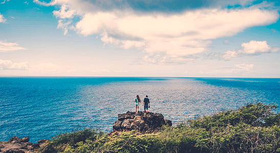 man and woman standing on cliff overlooking body of water thumbnail