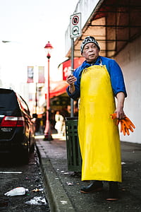 man in yellow apron holding orange gloves standing on sidewalk thumbnail