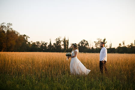 Groom Standing Next to Bride Holding Bouquet of Flower on Grass Field thumbnail