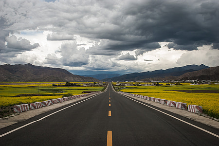 gray concrete road between grass fields under cumulus clouds thumbnail