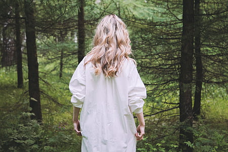 standing woman wearing white long-sleeved shirt in front of trees thumbnail