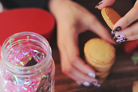 person holding baked cookies near clear glass cookie container thumbnail