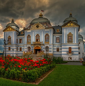 photo of brown and blue stone house near red petaled flowers thumbnail