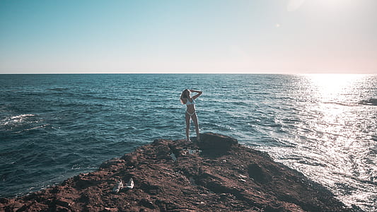 woman standing on rock formation near body of water thumbnail