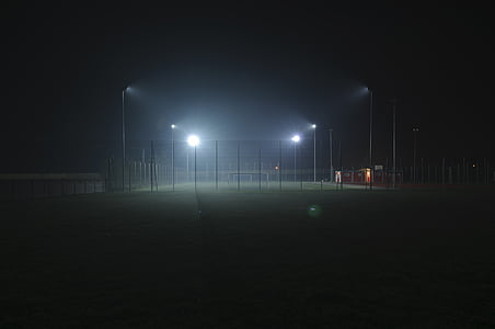 lights turned on in green field surrounded with fence at nighttime thumbnail