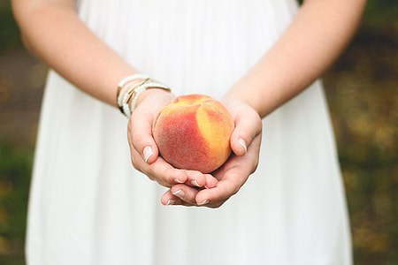 woman in white dress holding peach thumbnail