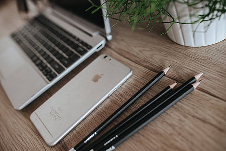 Silver Acer laptop on a wooden desk with a green plant, pencils and an Apple iPhone thumbnail