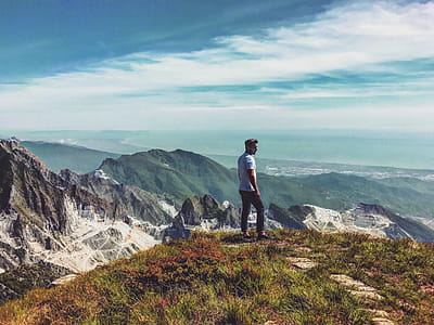 Man Wearing White T-shirt Standing on Mountain Under Blue Cloudy Sky thumbnail