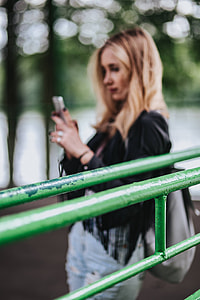 Blonde woman in a black jacket and ripped jeans by a green handrail thumbnail