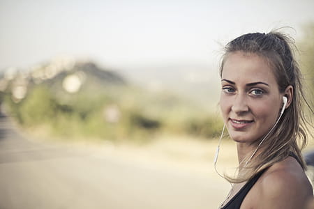 Young Woman In Black Tank Top And White Earbuds Looking At Camera thumbnail