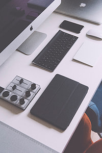 silver iMac, Apple cordless keyboard, traction pad, silver Macbook, and tablet case on white table thumbnail