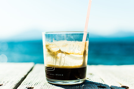 clear rocks glass filled black coffee with straw on wooden dock thumbnail