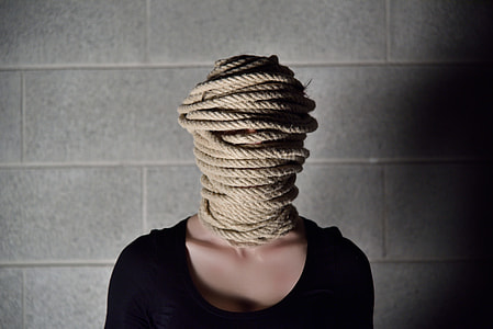 woman in black scoop-neck top and face covered with brown rope thumbnail