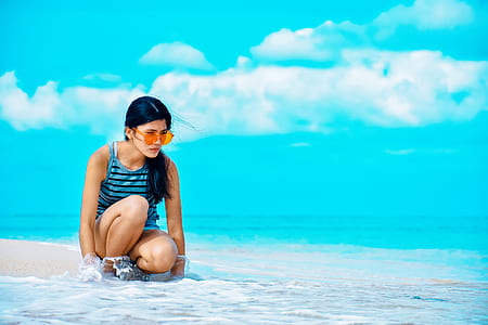 woman sitting on seashore under blue sky during daytime thumbnail