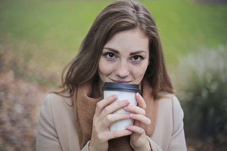 Woman in Brown Top and Scarf Holding a White and Black Travel Cup Outside thumbnail
