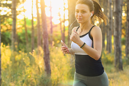 Girl jogging/running exercises workout in the forest using earphones connected to her mobile iPhone smartphone thumbnail