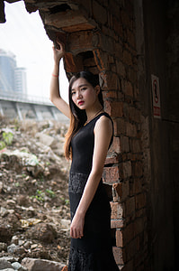 Woman in black sleeveless dress beside brown bricked wall thumbnail