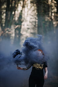 woman holding black smoke flare under shade of trees at daytime thumbnail