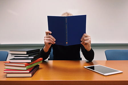person holding blue book leaning on brown wooden desk thumbnail