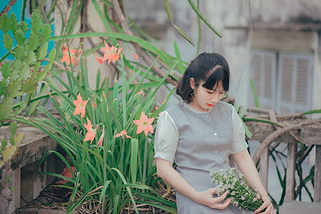Woman Sitting Beside Pink Petaled Flower While Holding Bouquet of Flower thumbnail