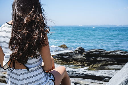 woman sitting on rock facing sea during daytime thumbnail