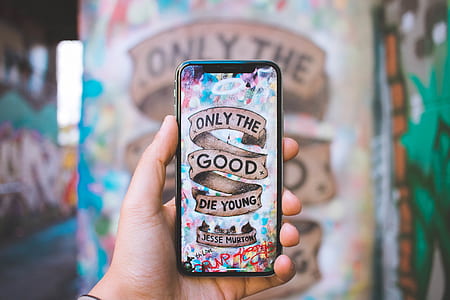 person holding silver iPhone X with only the good die young photo thumbnail